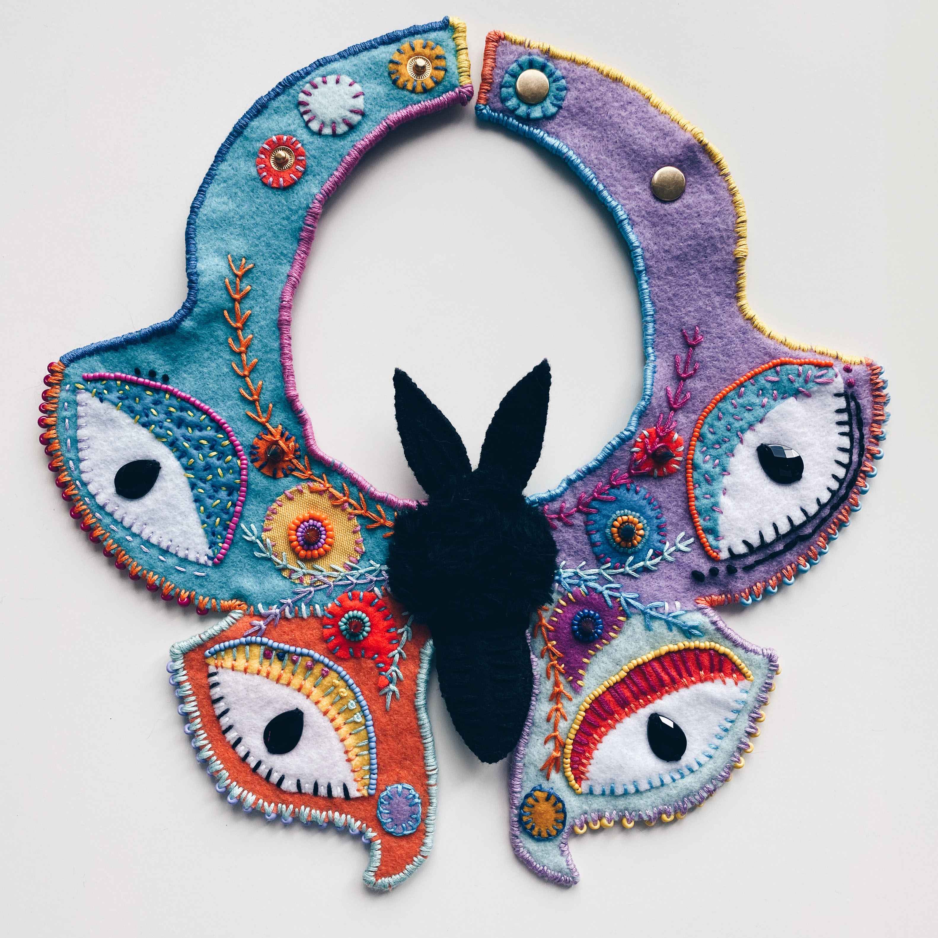 hand sewn fuzzy black moth necklace with large, colorful, beaded eye wings.