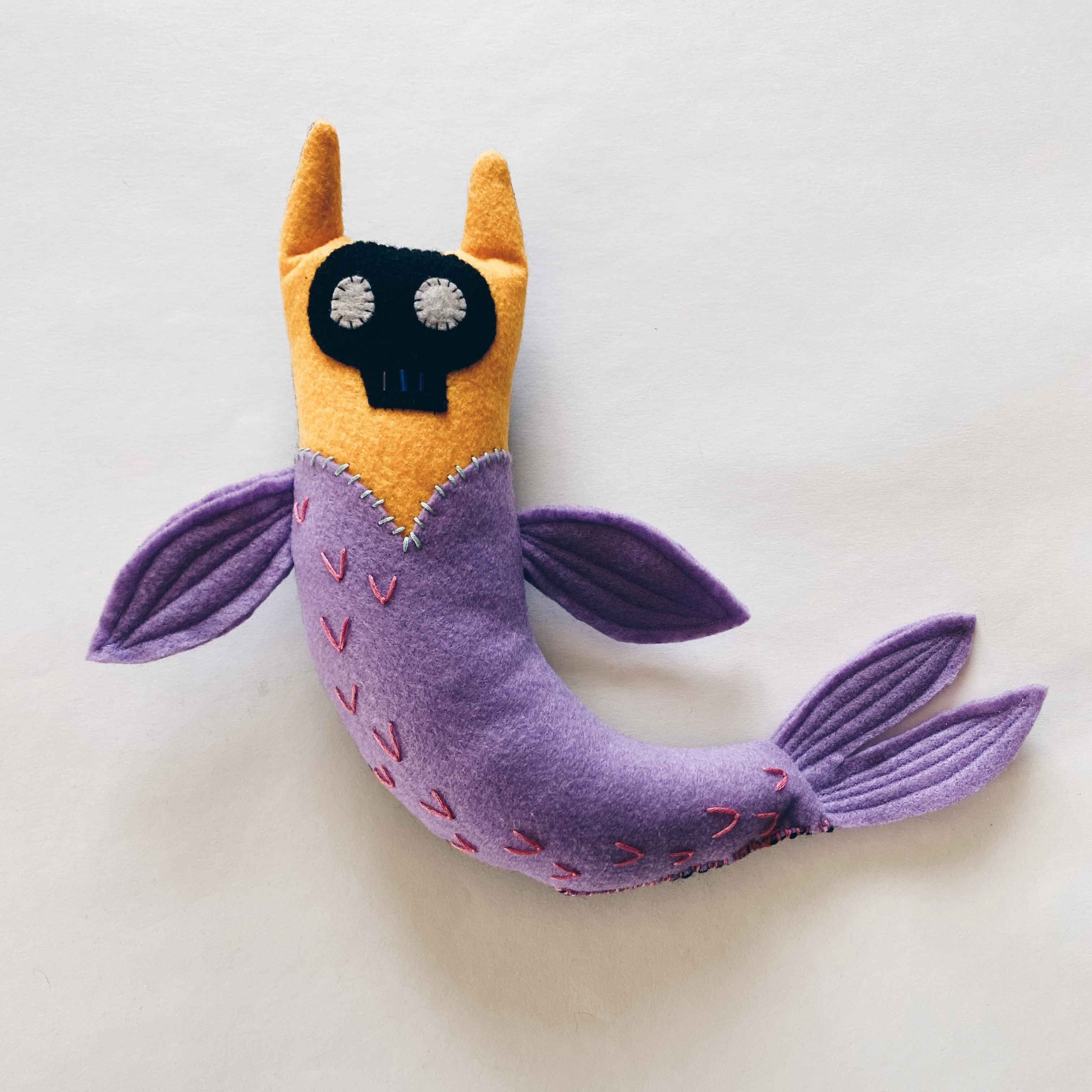 yellow and purple handmade catfish mermaid toy with black skull face and flippers.
