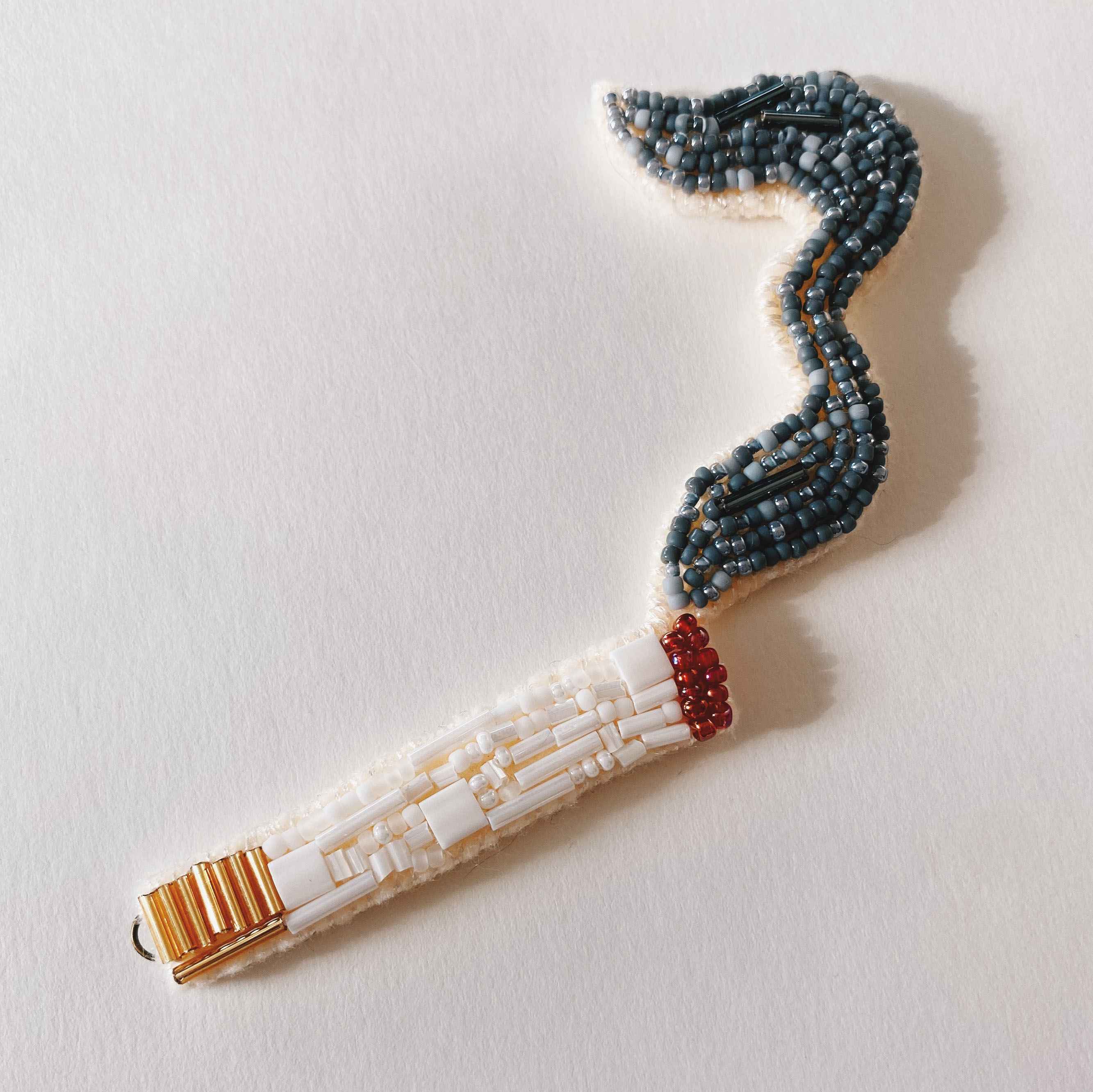 hand sewn seed bead embroidered cigarette with beaded smoke rising from the beaded burning ember.