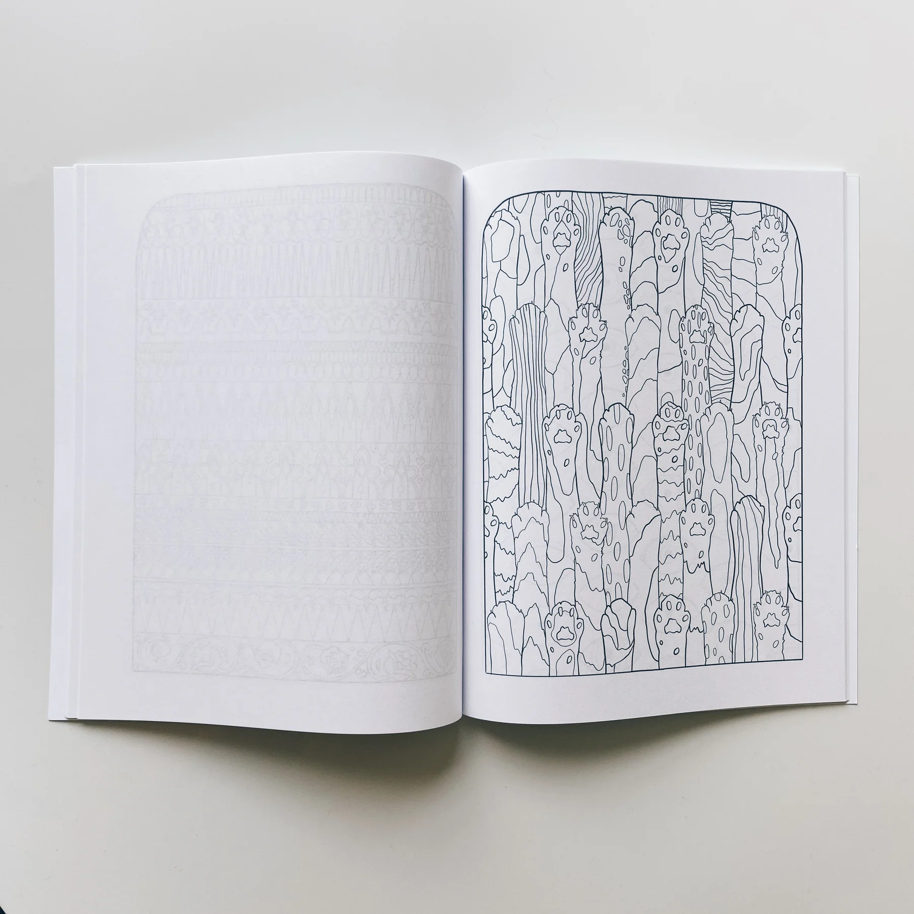 interior page of weird lizas colorama volume 2 with illustration of cat paw pattern. page is uncolored, book open on white background.