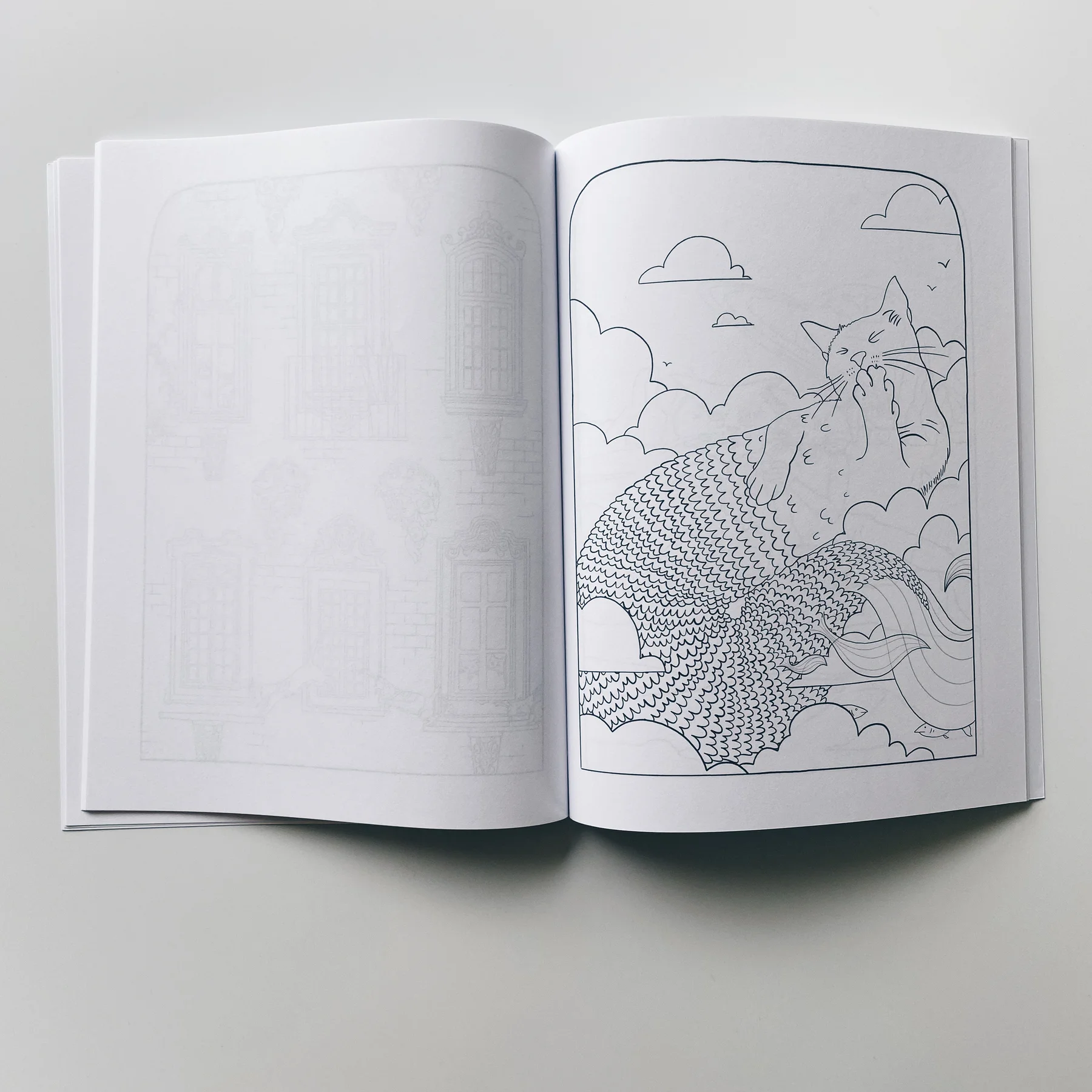 interior page of weird lizas colorama volume 4 with illustration of cat mermaid relaxing in a cloud. page is uncolored, book open on white background.