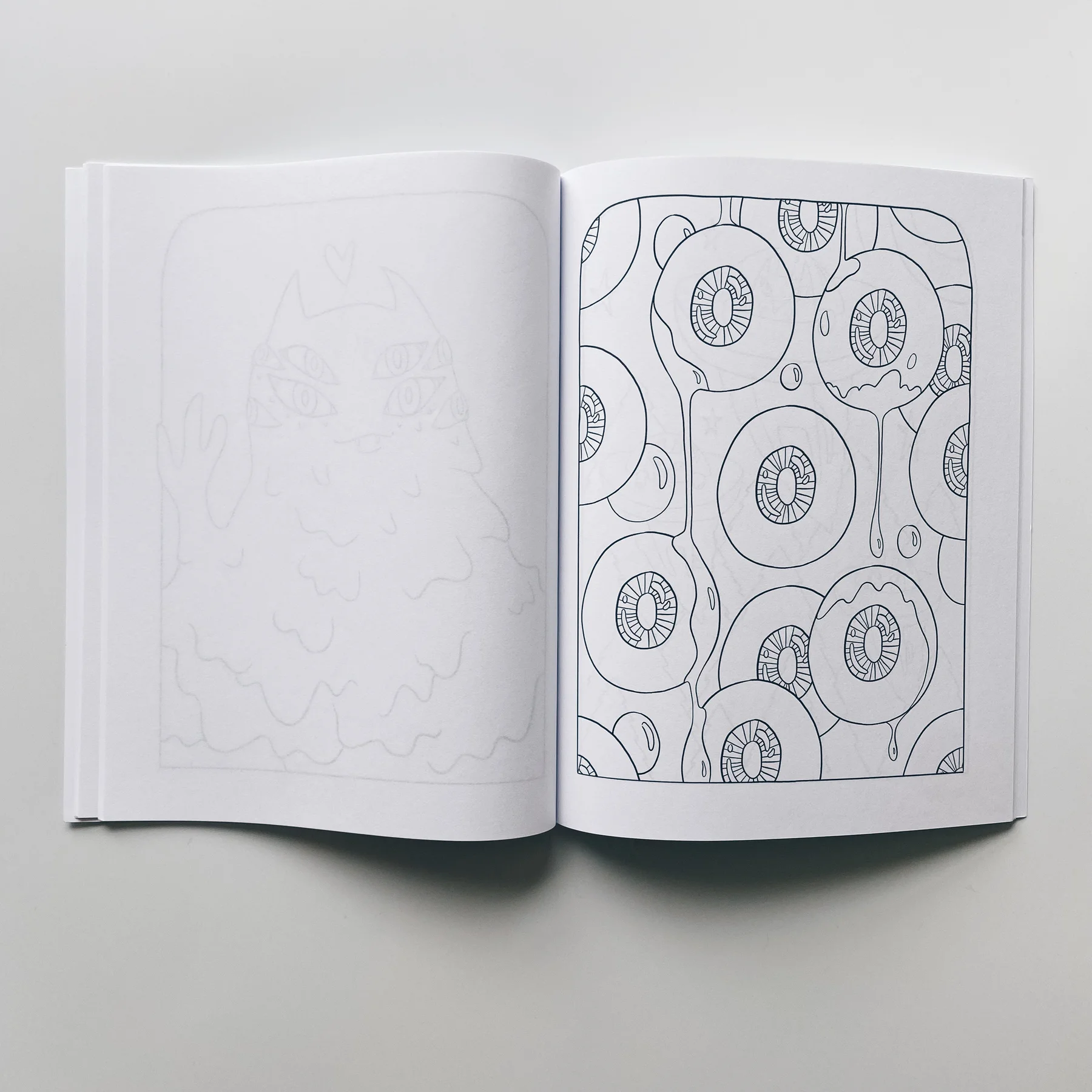 interior pages of weird lizas colorama volume 7 with large round monster eyeballs dripping with goo. page is uncolored, book open on white background.