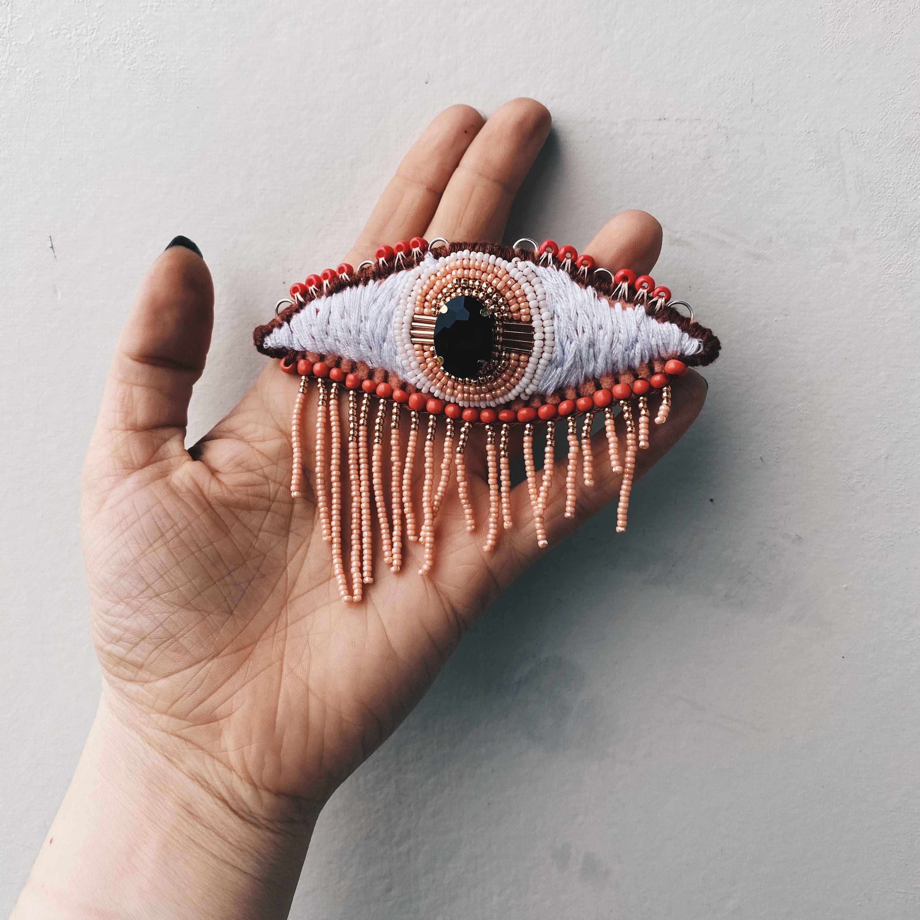 bead embroidered eye and beaded fringe hanging down, held in hand for scale.