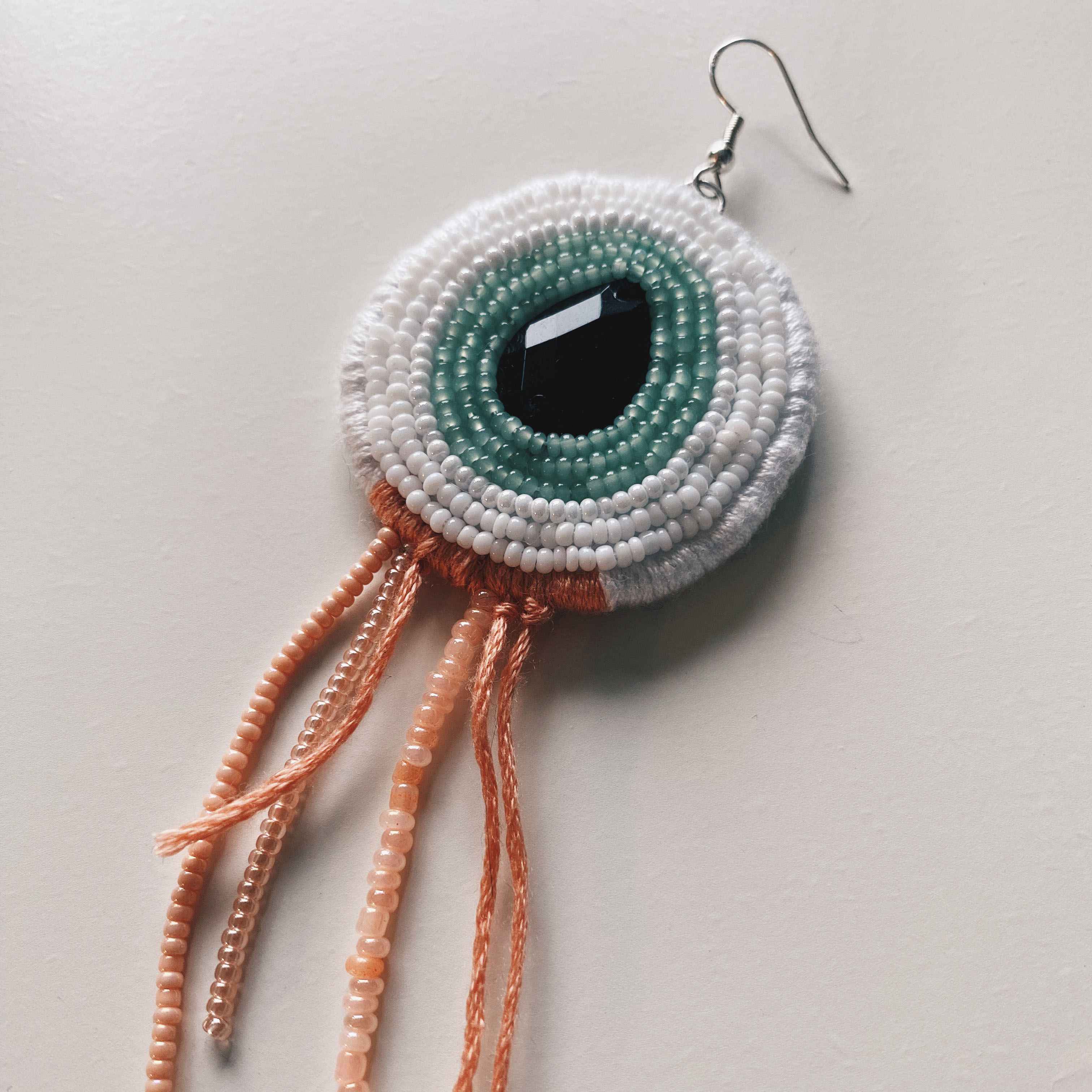 hand embroidered beaded earring with green iris and pink beaded tentacles hanging down.