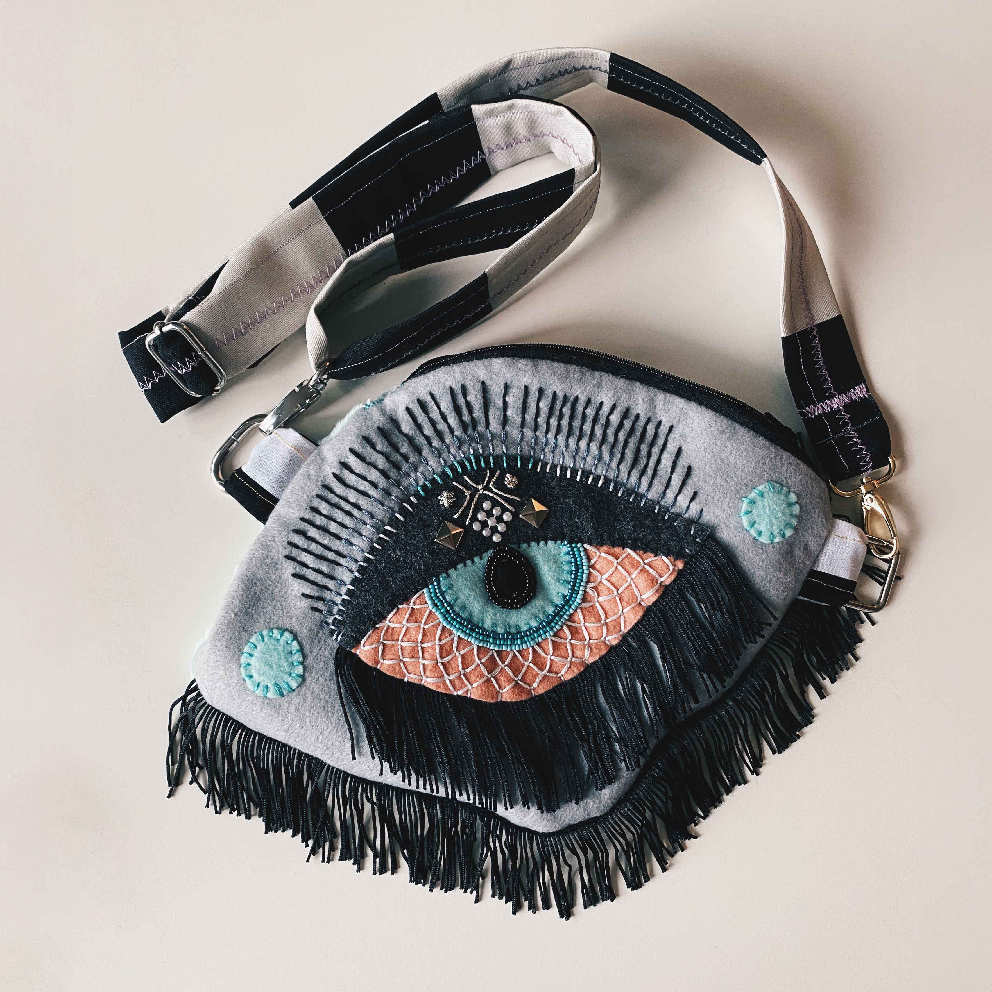 handmade gray fanny pack with beaded embroidered eye, fringe and strap.