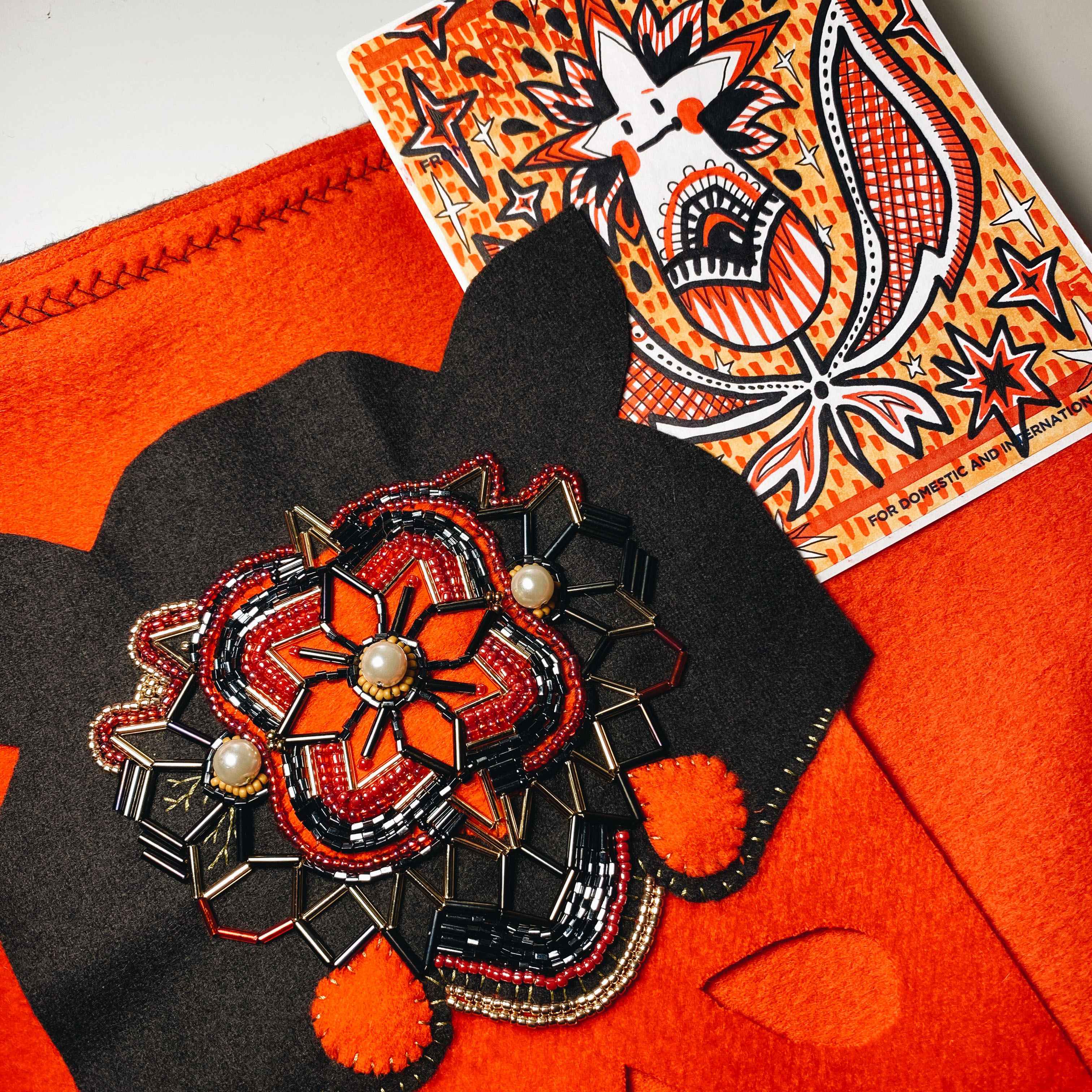 work in progress: black and red flower or star shaped symmetrical intricate beading. Shown with sticker drawing of a red and white star coming out of a flower.