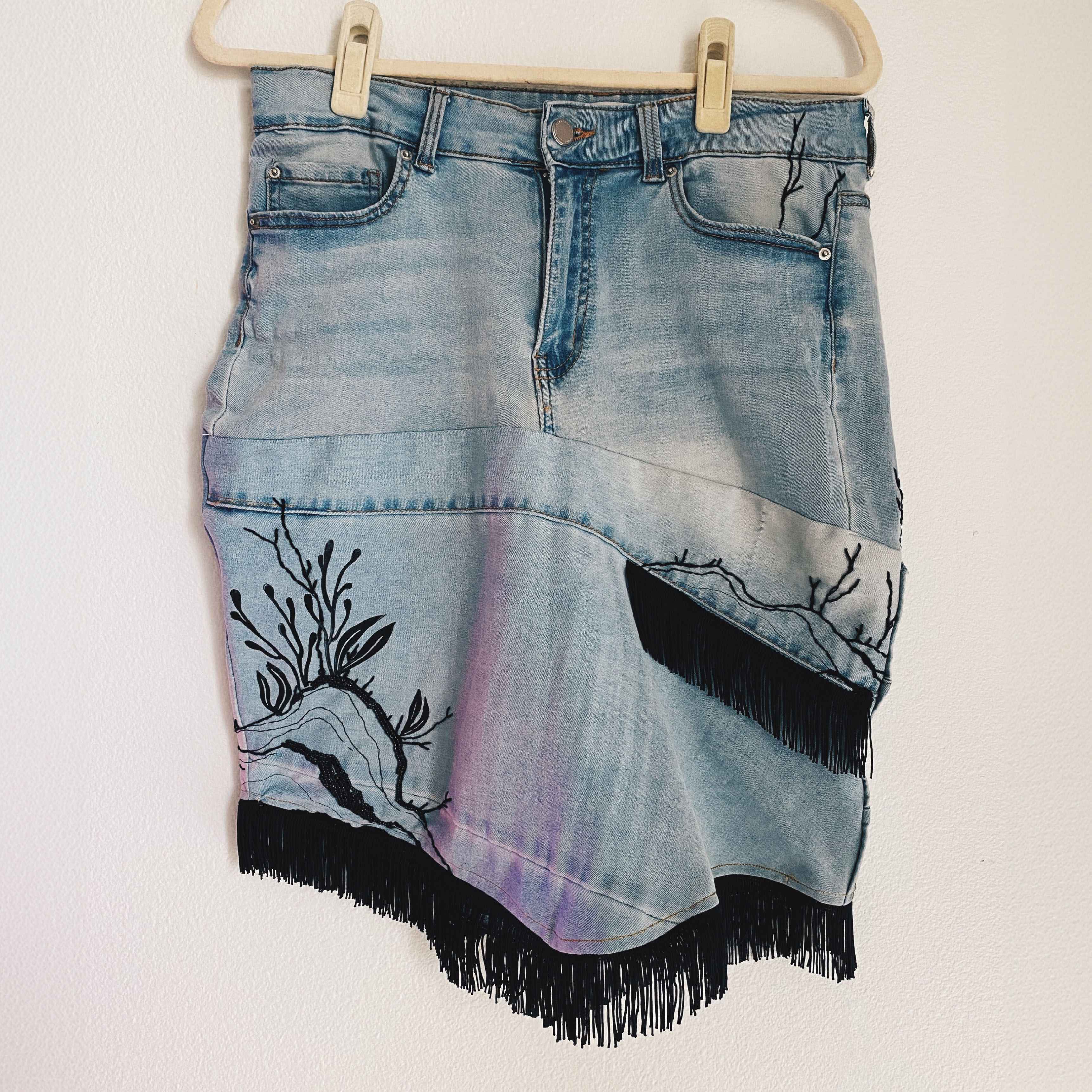 Jean skirt hand cut and stitched from salvaged fabric. Hand embroidery, lino blocking and beading. Black fringe along bottom and as accent.
