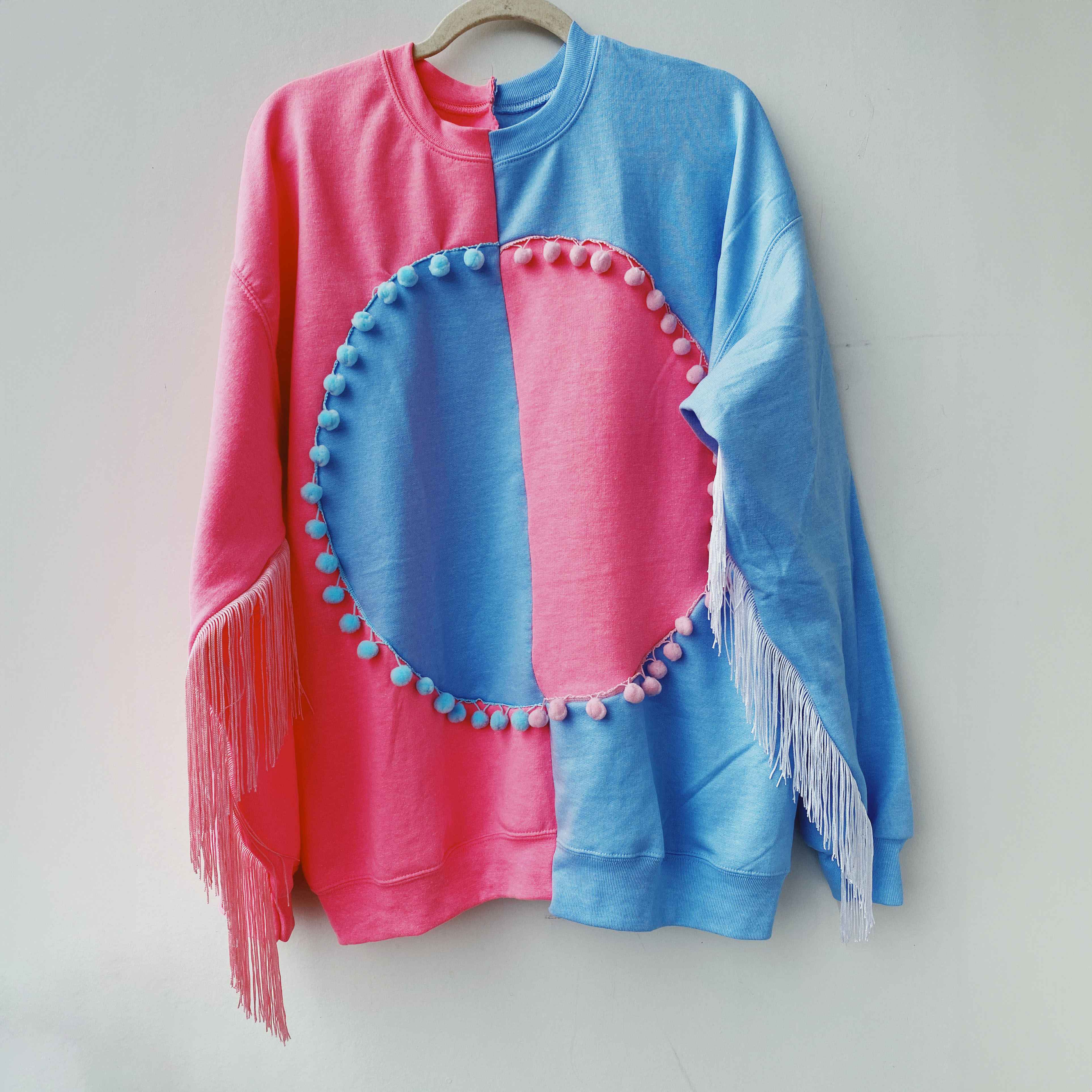 two tone sweatshirt sewn with pom poms around large center circle and matching fringe on each sleeve.